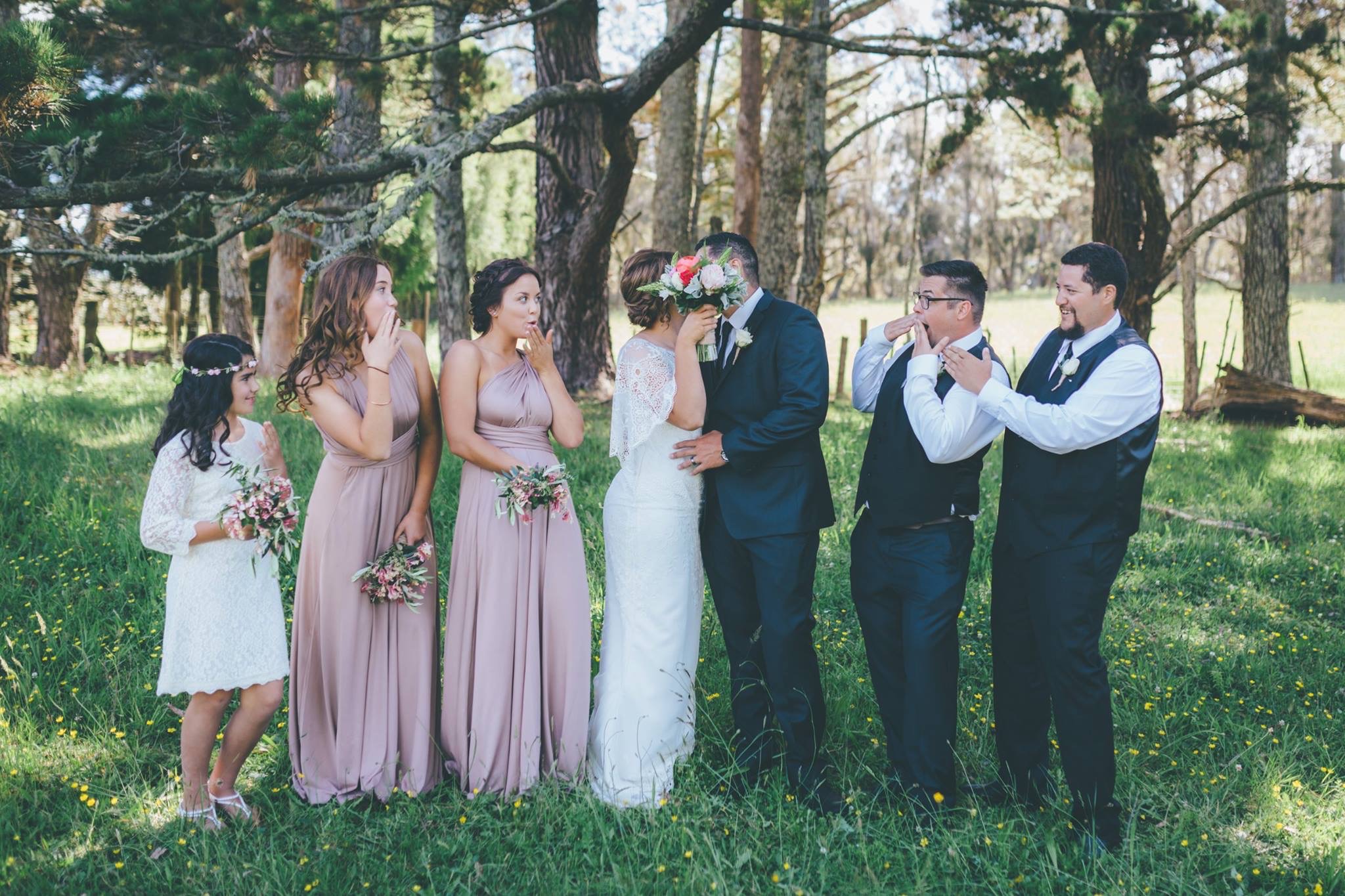 Bride & groom kissing behind flowers and wedding party 