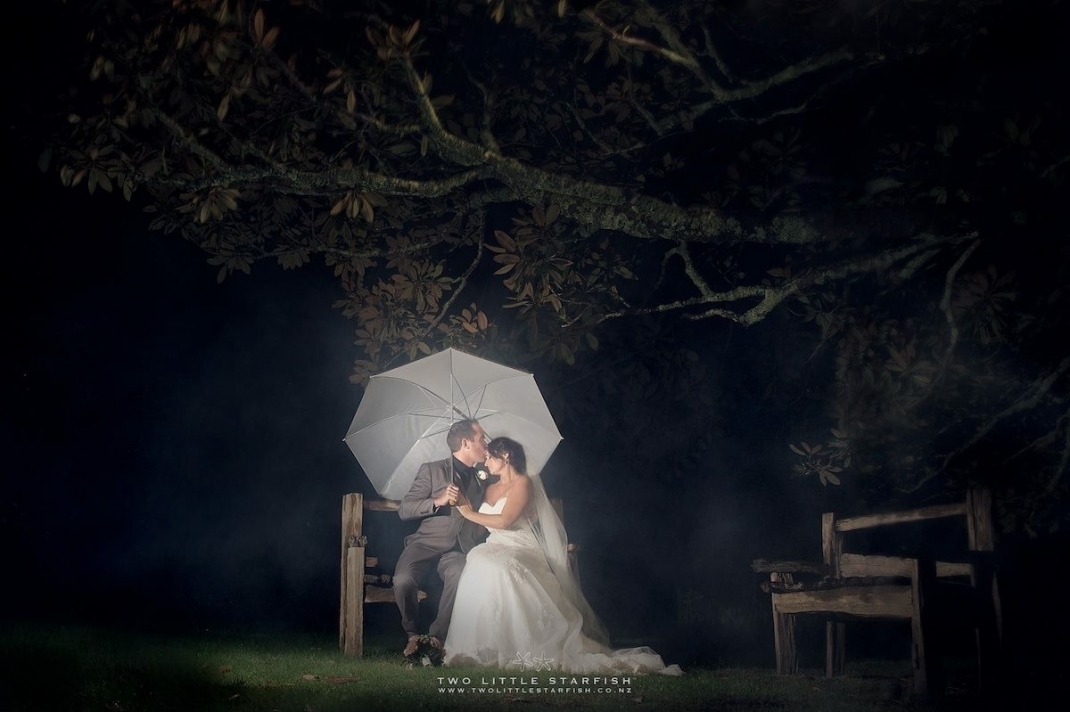 Bride and groom sitting in gardens under umbrella. Hair Laurel Stratford, bay of Islands NZ