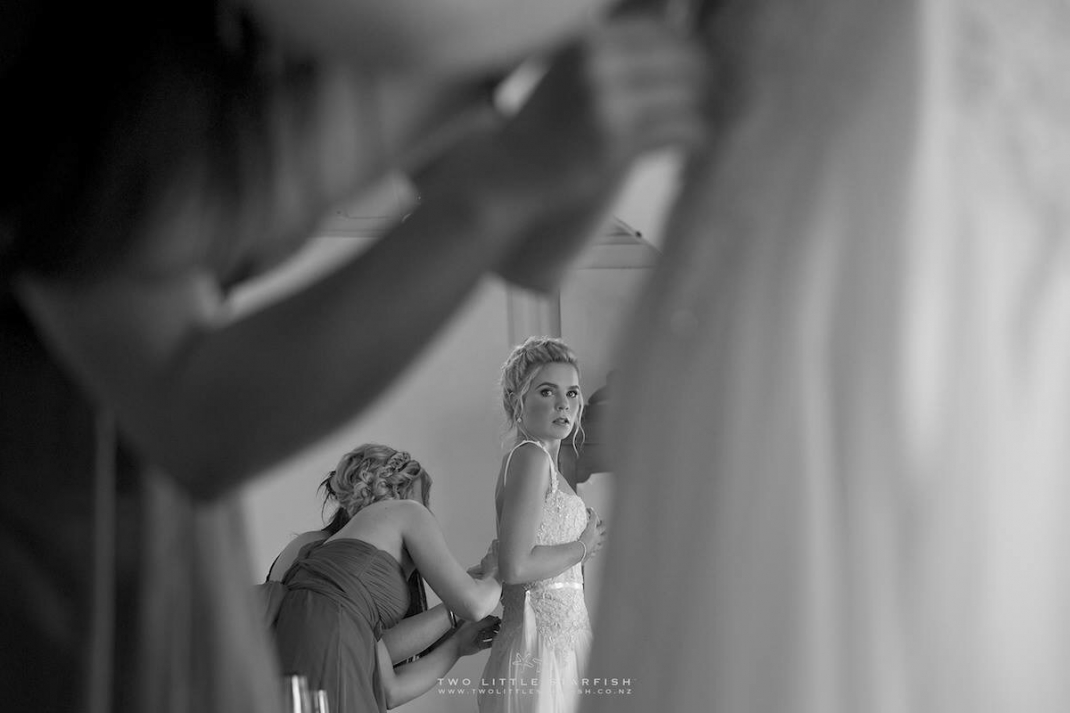 Bridesmaid adjusting bridal gown while bride looks in mirror, hair LaurelStratford hairstylist